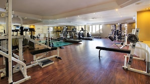 Une salle de sport spacieuse, dotée de divers appareils d’exercice, de grandes fenêtres et d’un plancher en bois.
