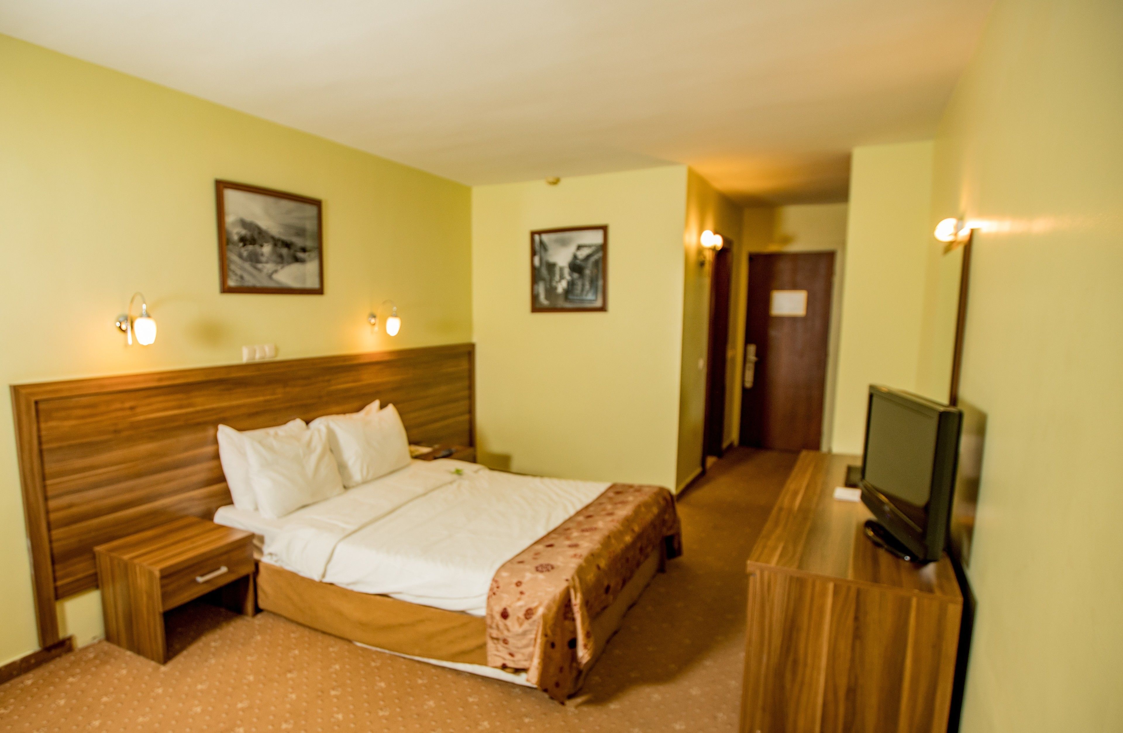Ein Hotelzimmer mit einem hölzernen Bett, Nachttischen, einem Fernseher und gerahmten Bildern an den Wänden.
