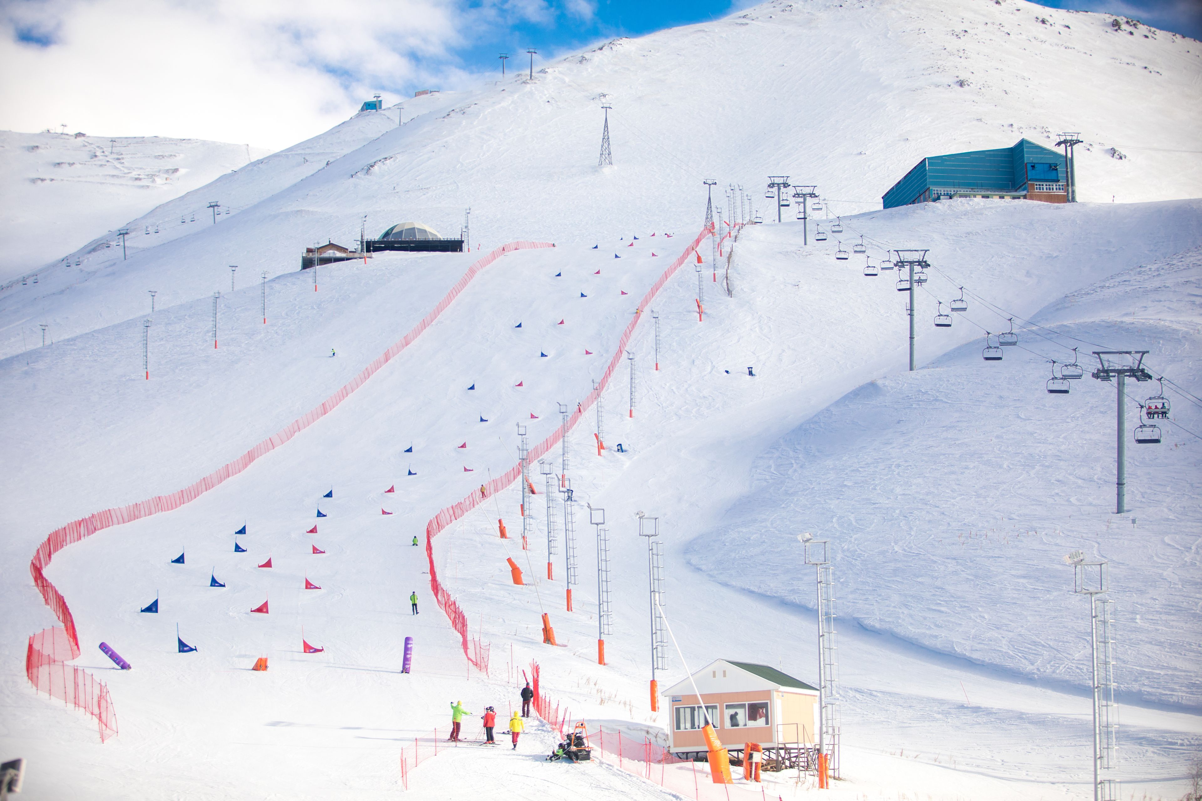 Una pista de esquí con un telesilla, un pequeño edificio y una montaña cubierta de nieve.
