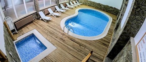A pool area with a hot tub, lounge chairs, and a stone wall.