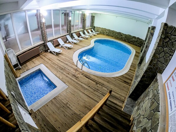 A pool area with a hot tub, lounge chairs, and a stone wall.