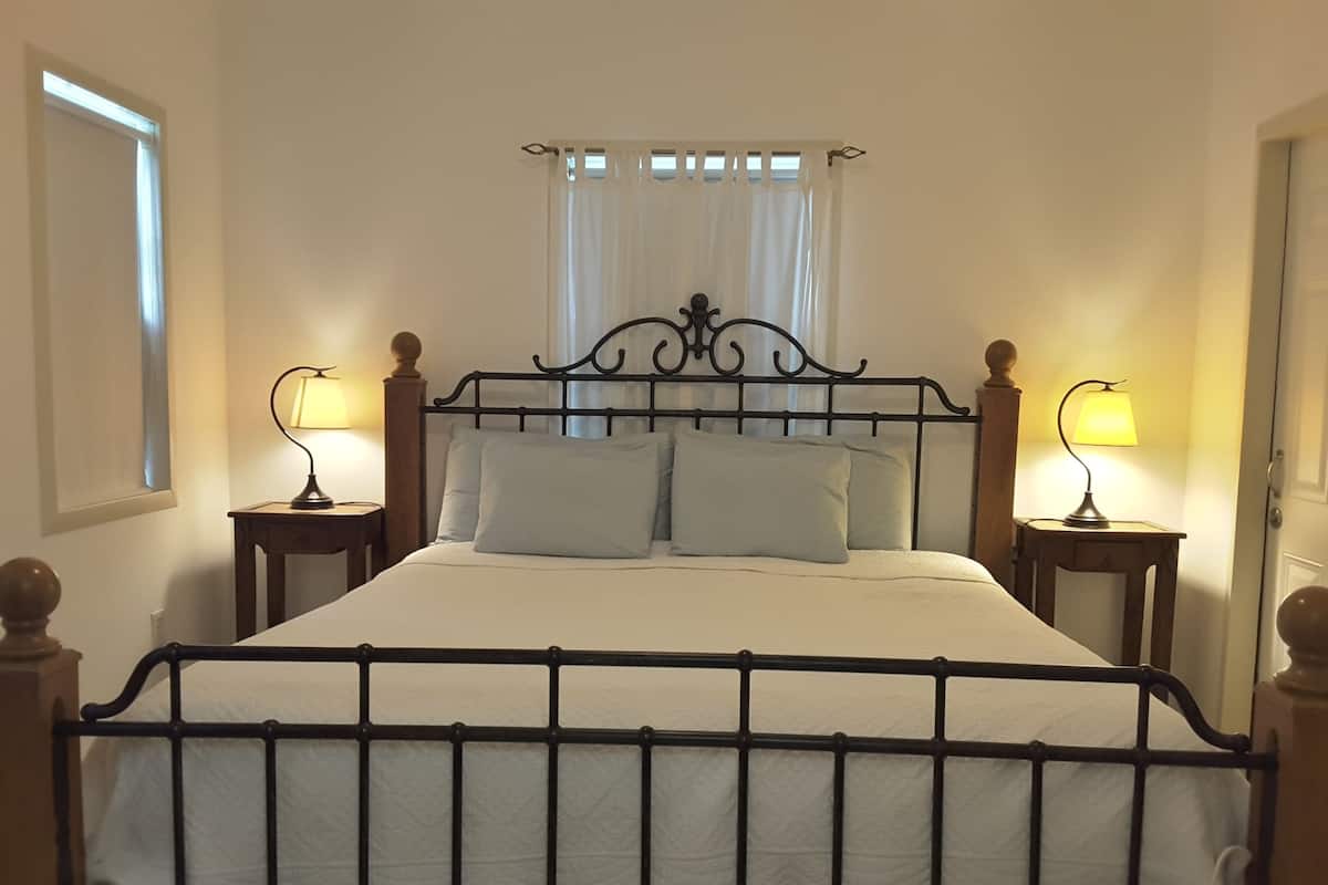 A bed with a metal frame, two bedside tables, and a window with white curtains.