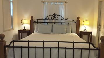 A bed with a metal frame, two bedside tables, and a window with white curtains.