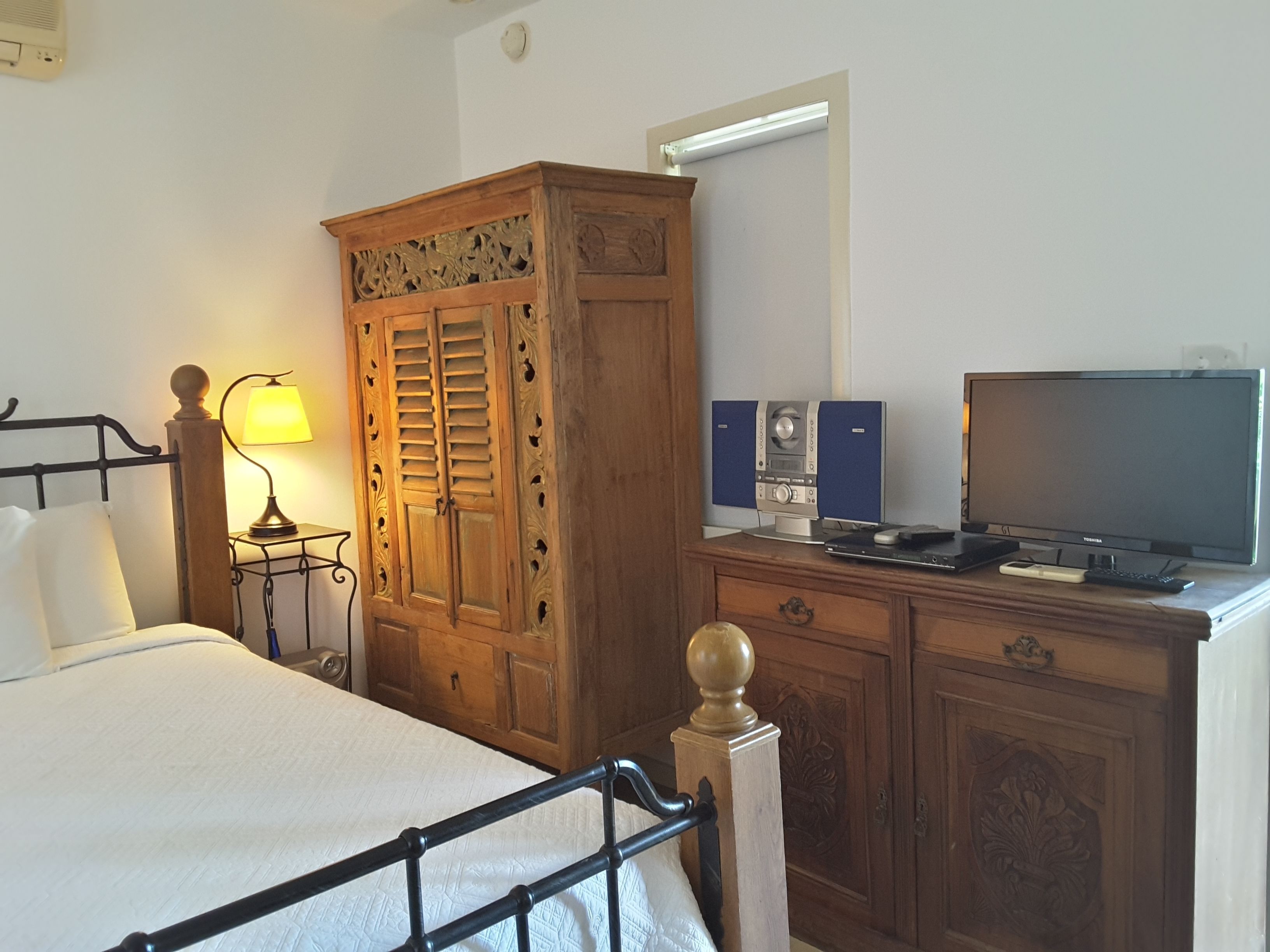 Une chambre à coucher comprenant un lit, une armoire en bois, une table de chevet avec une lampe, une télévision et des haut-parleurs.