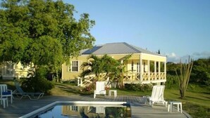 A house with a pool, surrounded by greenery and a clear sky. - Yepton Estate Cottages (St. John's)