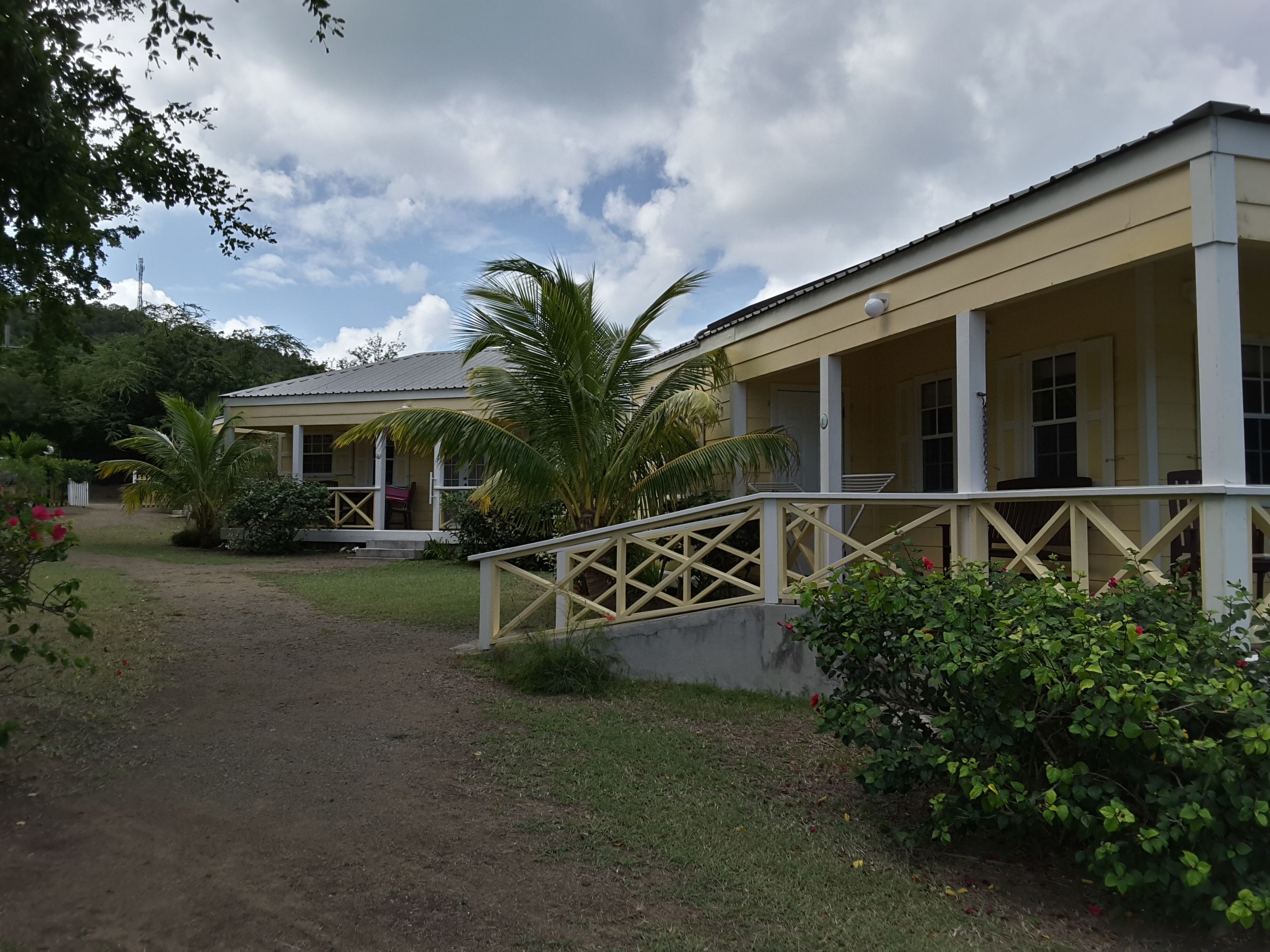 A two-story building with a covered porch and a small garden area with palm trees and shrubs.