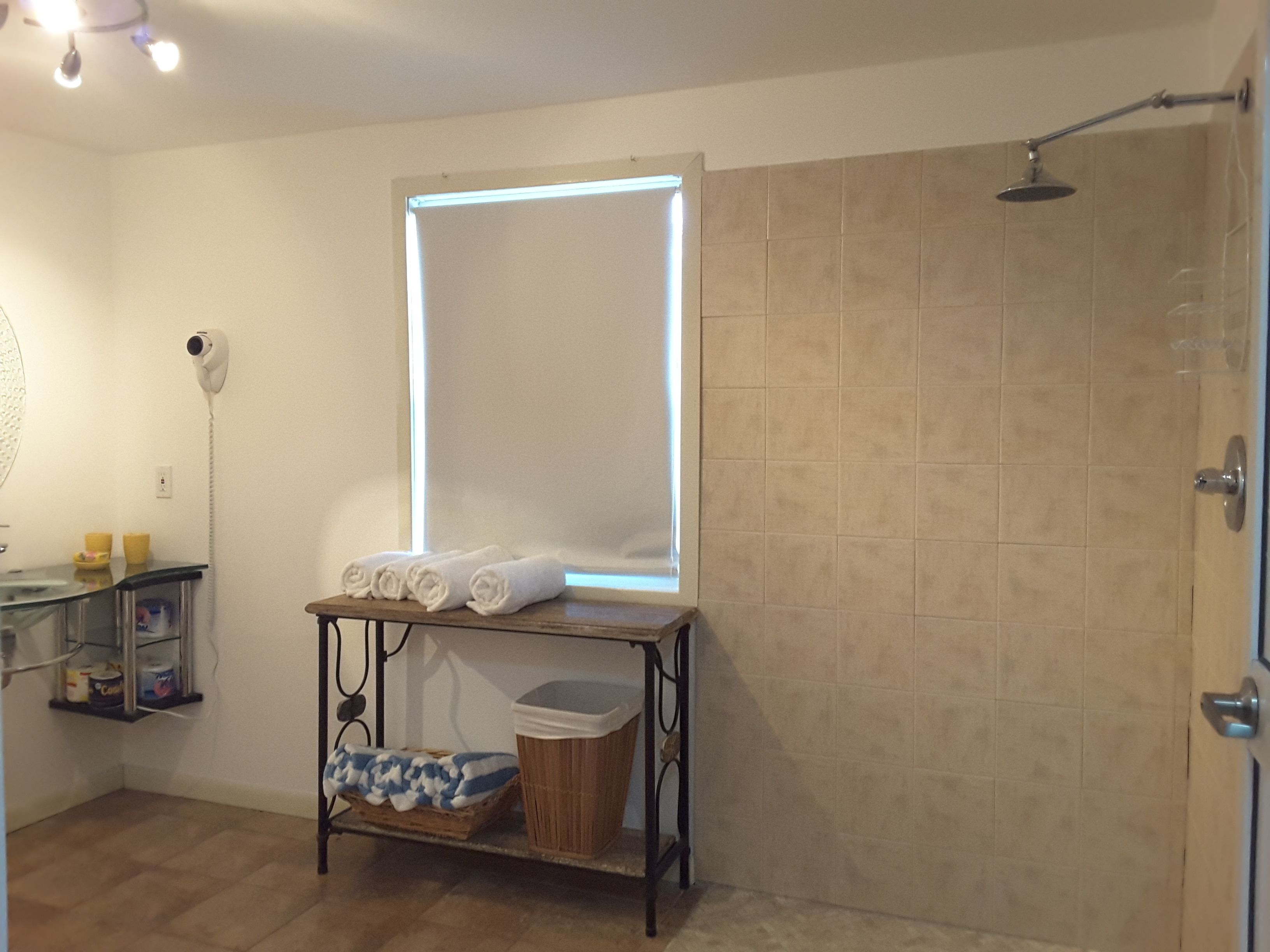 Ein Badezimmer mit Dusche, einem Spiegel, einem Handtuchhalter und einem kleinen Tisch mit einem Mülleimer.