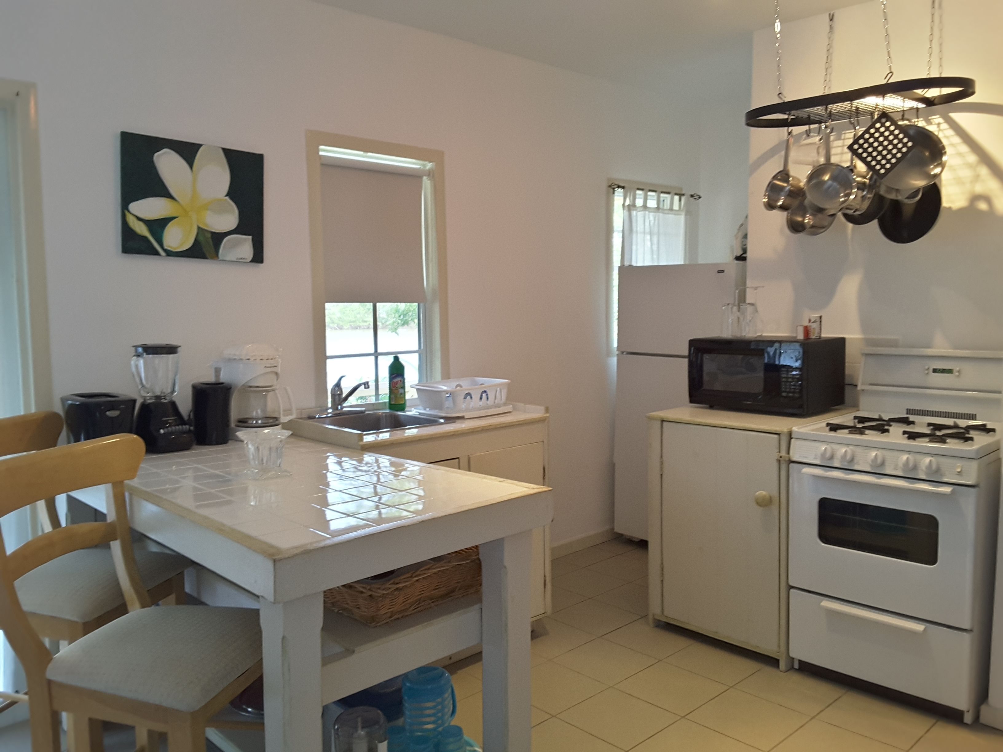 A small kitchen with white appliances, a dining table, chairs, and a window with curtains.