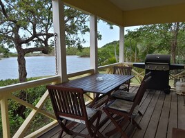 Un espacio al aire libre techado con una mesa y sillas de madera, una parrilla y vistas a un lago.