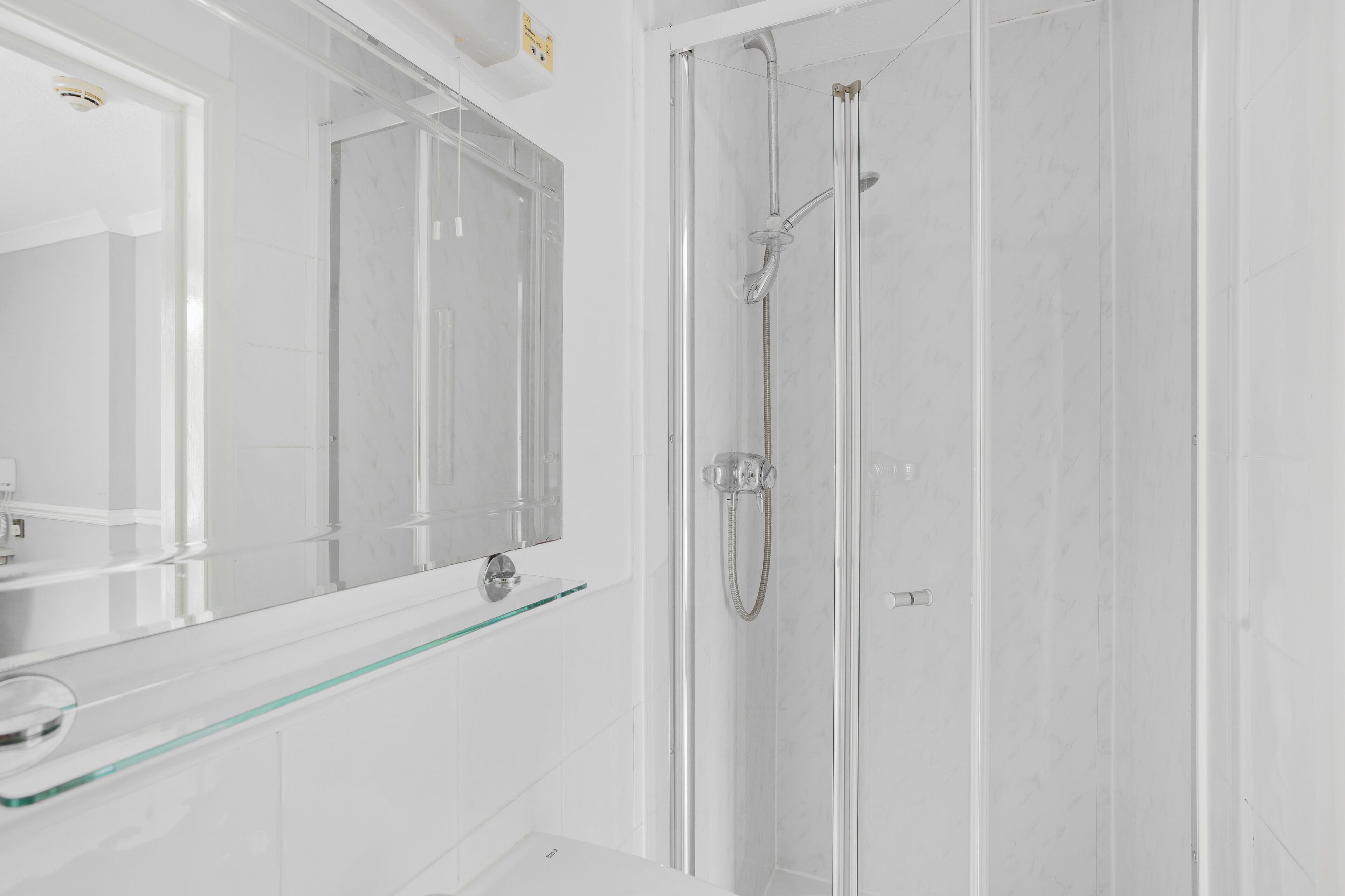 Een moderne badkamer met een douchecabine van glas, een wastafel met glazen blad en een grote spiegel.