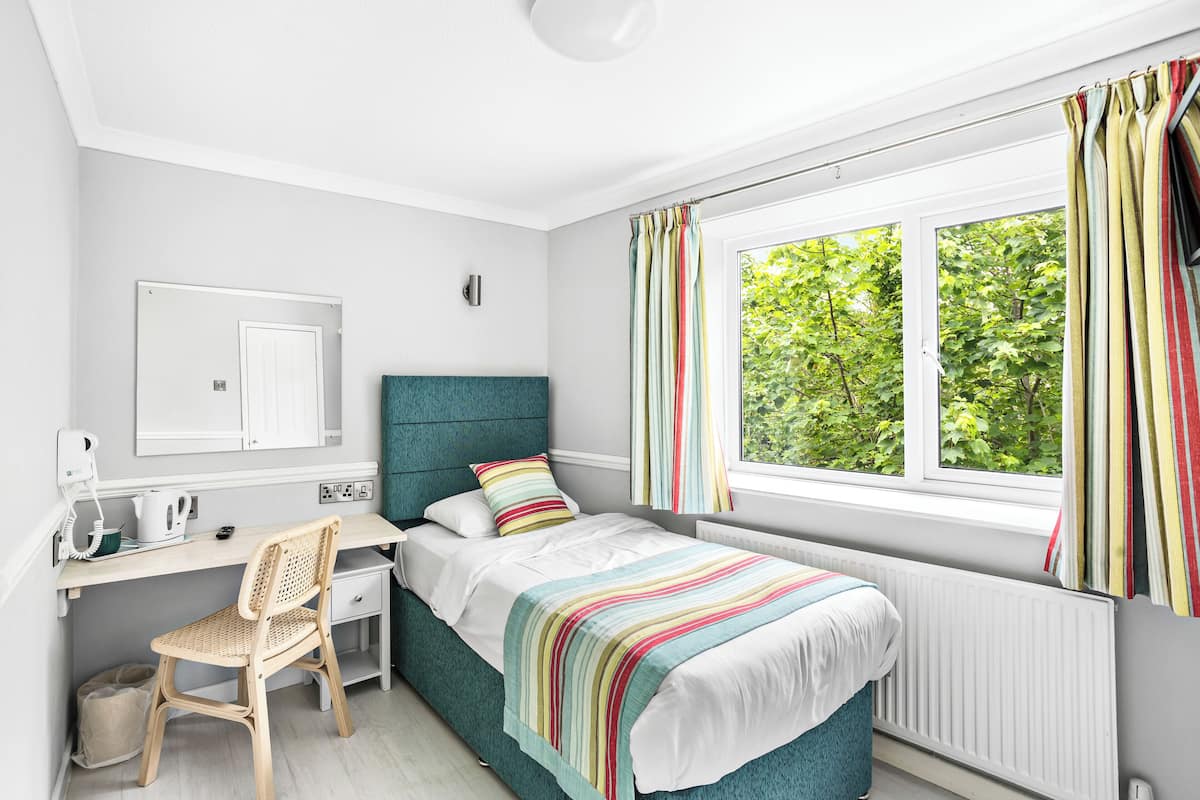 Une chambre à coucher avec un lit, un bureau, une chaise et une fenêtre avec des rideaux.