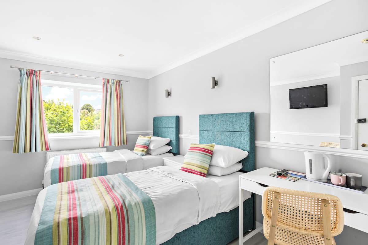 Une chambre avec deux lits, un bureau, une chaise, une télévision et une fenêtre avec des rideaux.