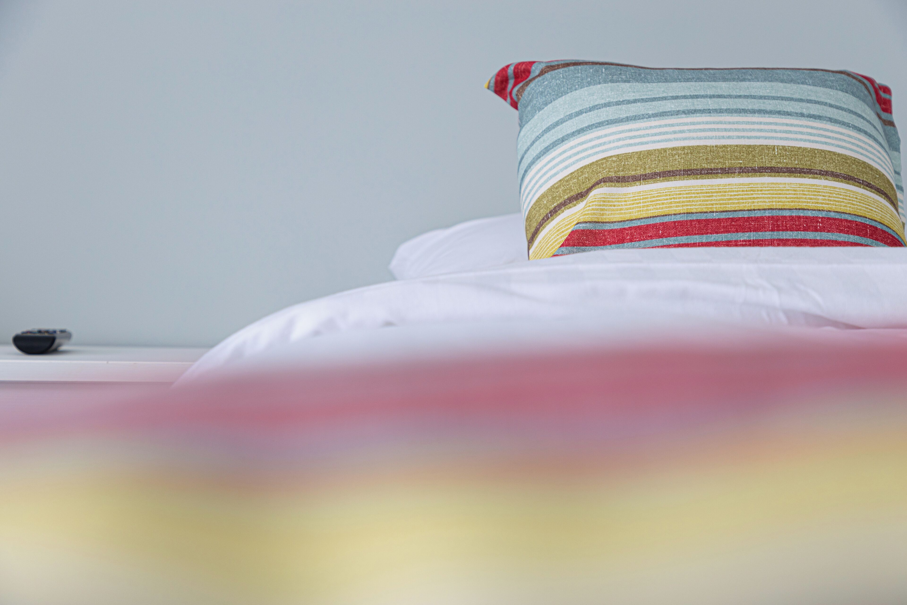 A bed with a striped pillow and white bedding.