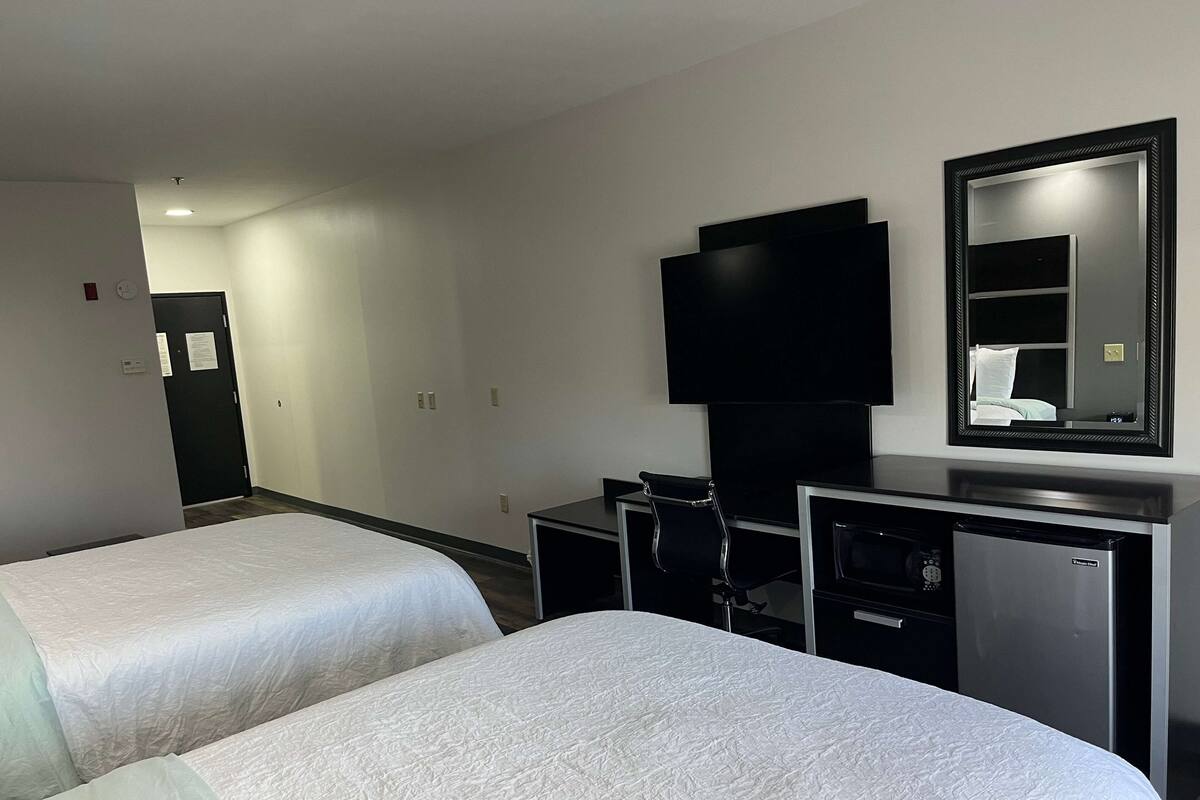 A hotel room with two beds, a desk, a chair, a television, and a refrigerator.