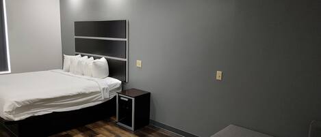 Un lit bien fait dans une pièce dont le mur est peint en gris foncé, avec une petite table de chevet et une étagère fixée au mur au-dessus du lit.
