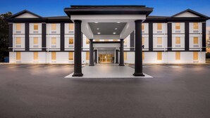 Entrada de hotel con un paseo techado, columnas y estacionamiento.