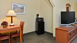 A hotel room with a wooden desk, a chair, a lamp, a television, a coffee maker, and a dresser. - Days Inn by Wyndham Abbeville (Abbeville)