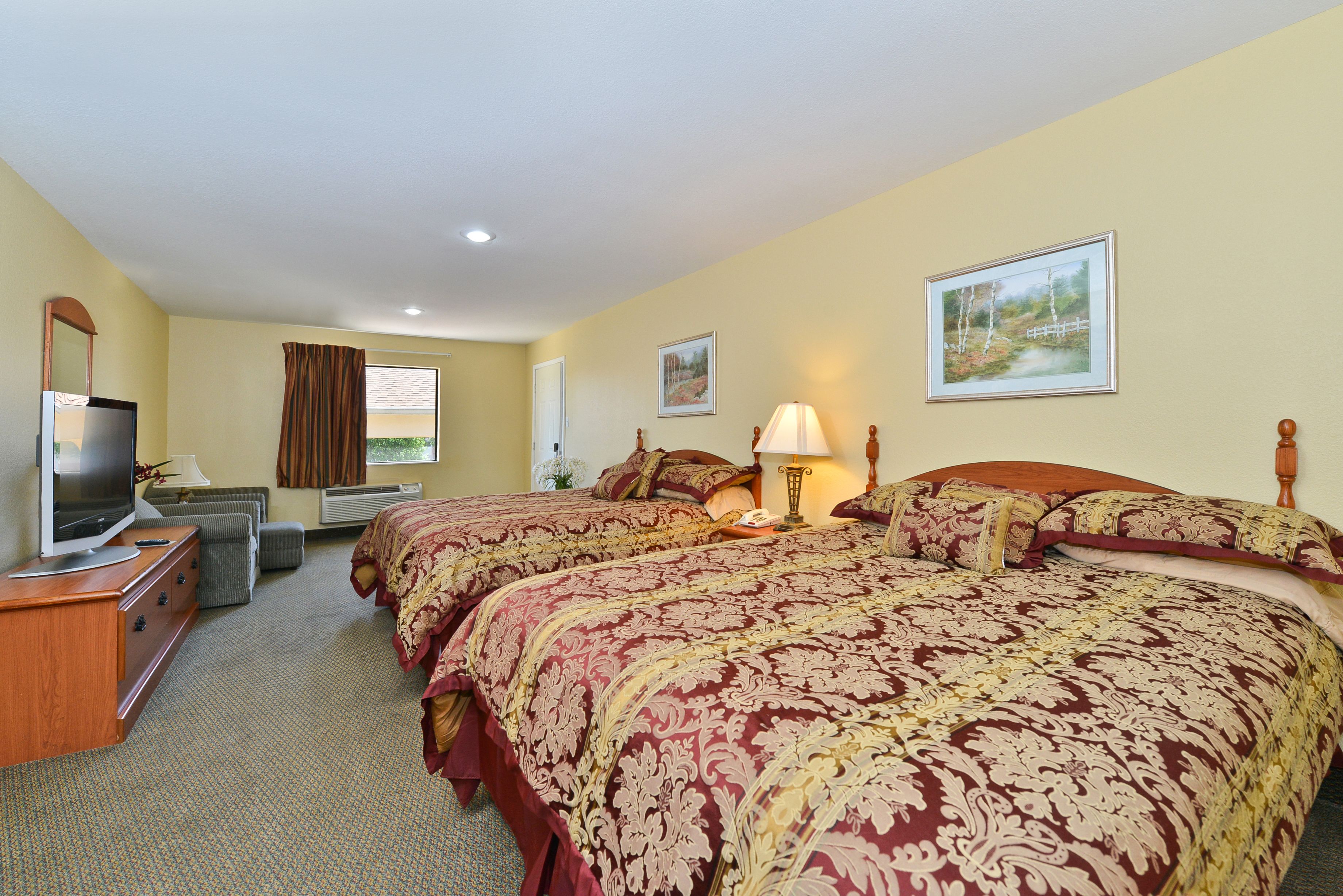A hotel room with two large beds, a television, a desk, and a window with curtains.