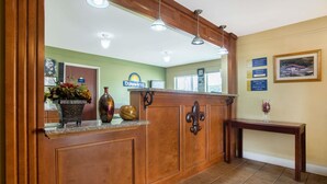 A reception area with a wooden counter, a vase with flowers, a sign for Days Inn, and a framed picture on the wall. - Days Inn by Wyndham Abbeville (Abbeville)