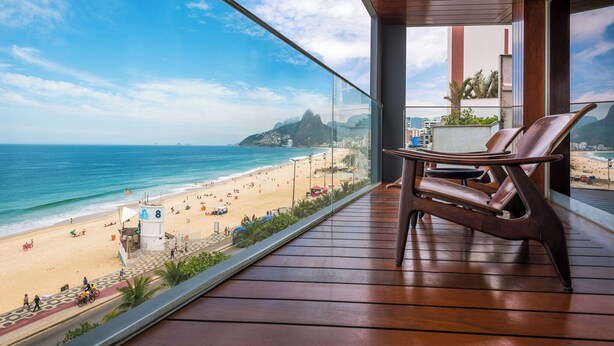 Un balcón con vista a una playa y al océano, piso de madera y dos sillas.