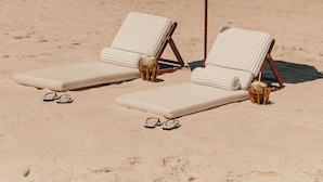 Dos sillas de playa con una sombrilla verde, situadas en una playa arenosa con olas del océano al fondo.