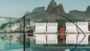 Un área junto a la piscina con sillones de descanso y plantas en macetas, que refleja el paisaje y las montañas circundantes.