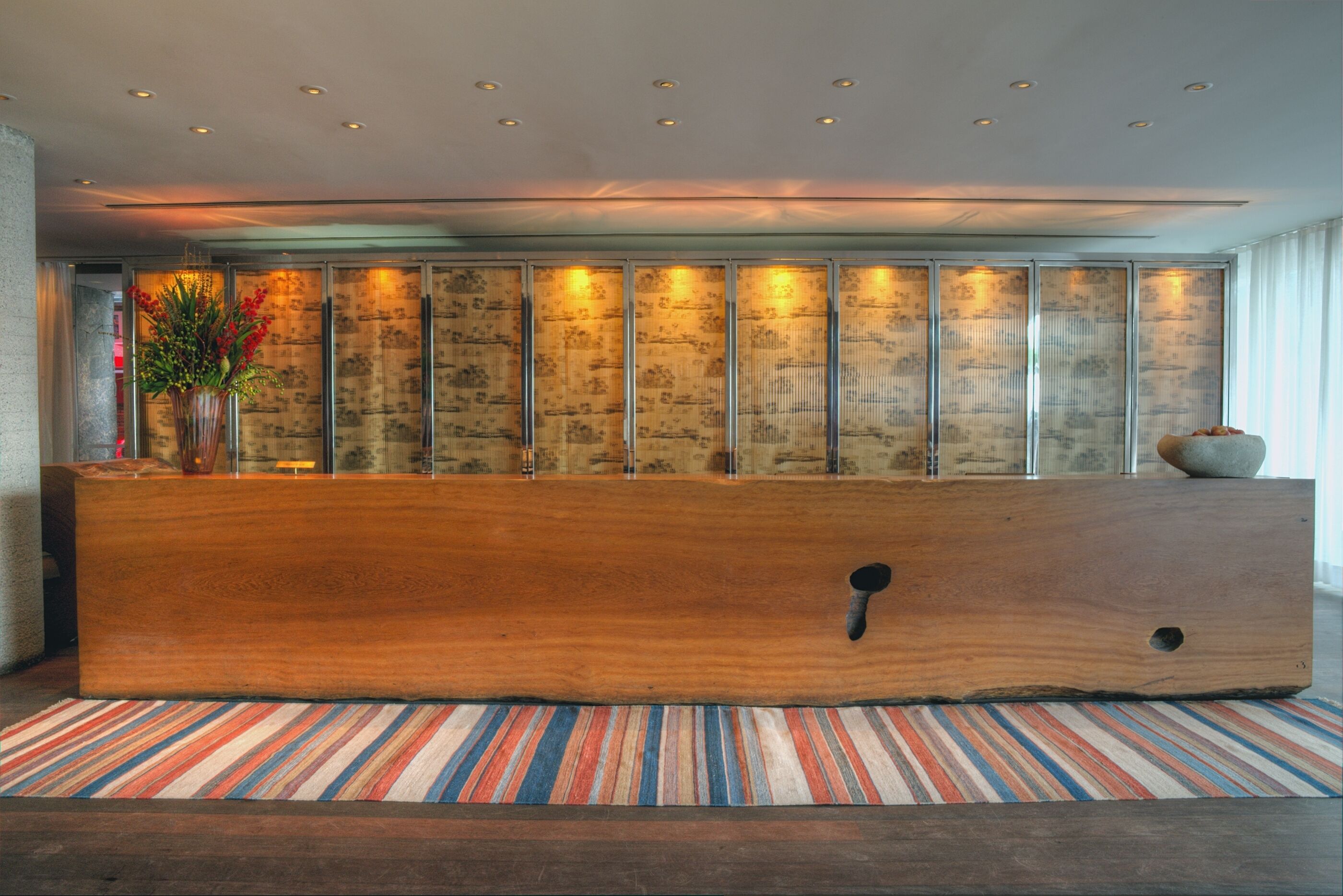 A reception area with a wooden reception desk, a striped rug, and a wall with vertical panels.