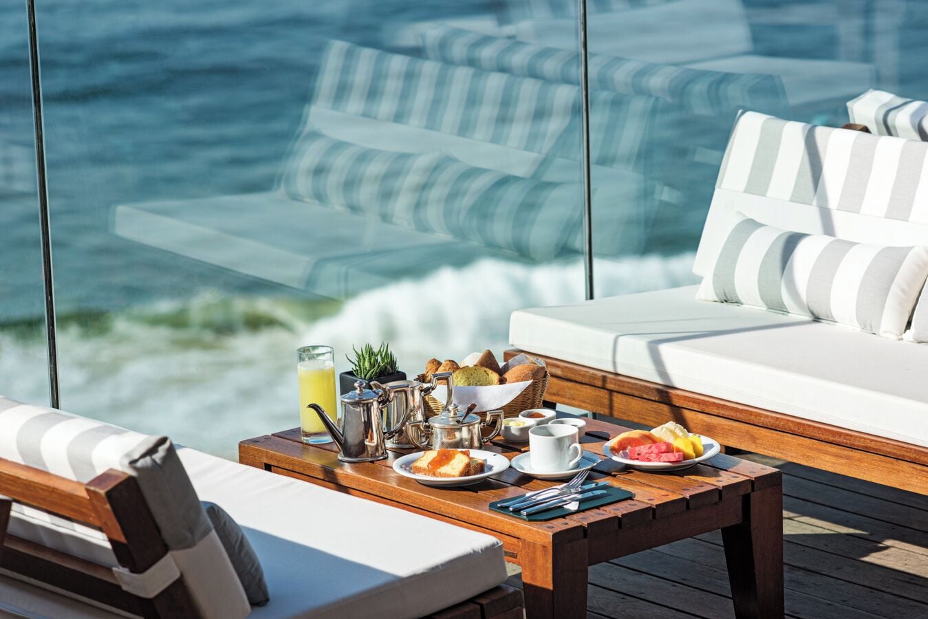 A wooden deck with a breakfast setup including a table, chairs, and a sofa with striped cushions.