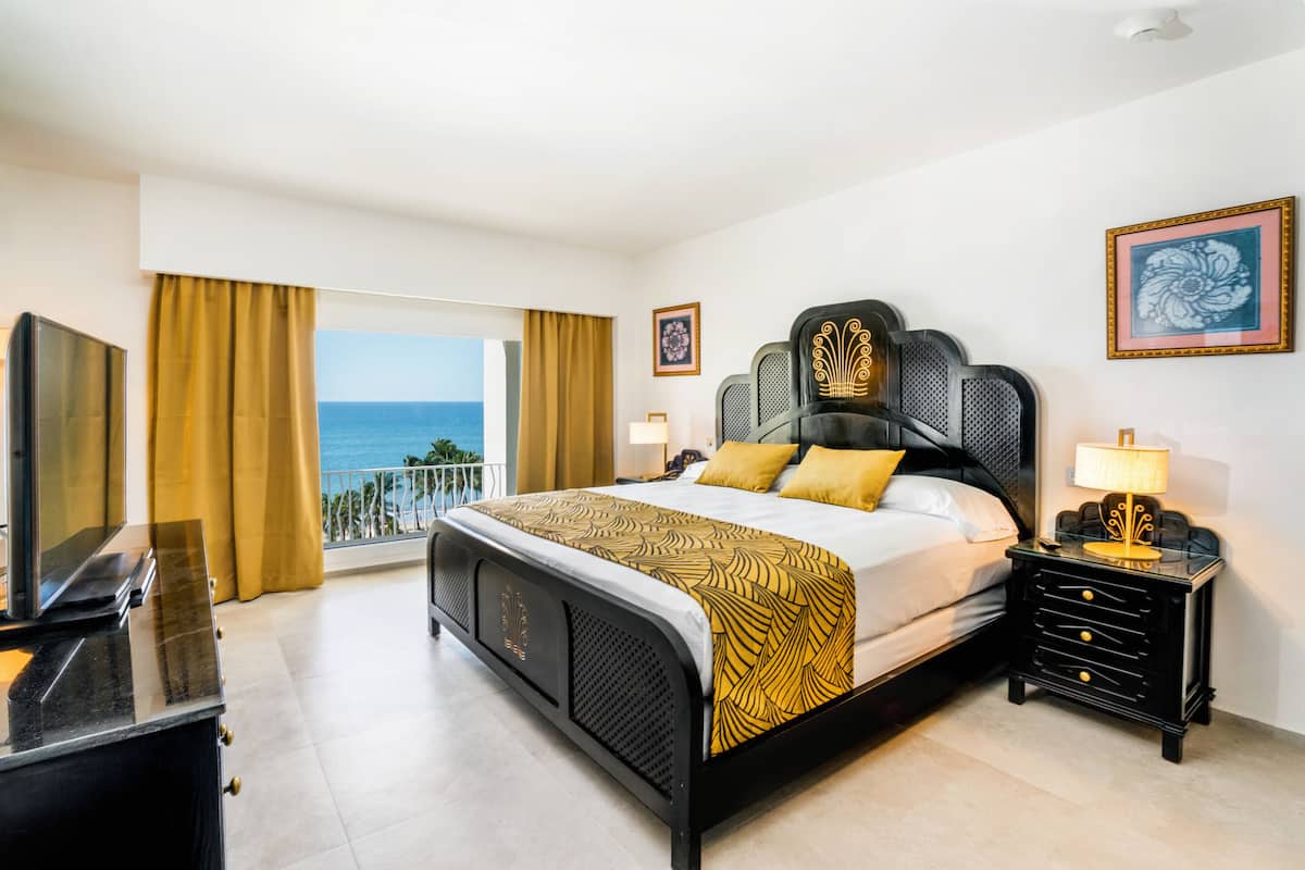 Habitación de hotel con cama, televisión, mesita de noche y vista al océano.
