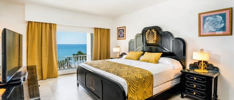 Habitación de hotel con cama, televisión, mesita de noche y vista al océano.