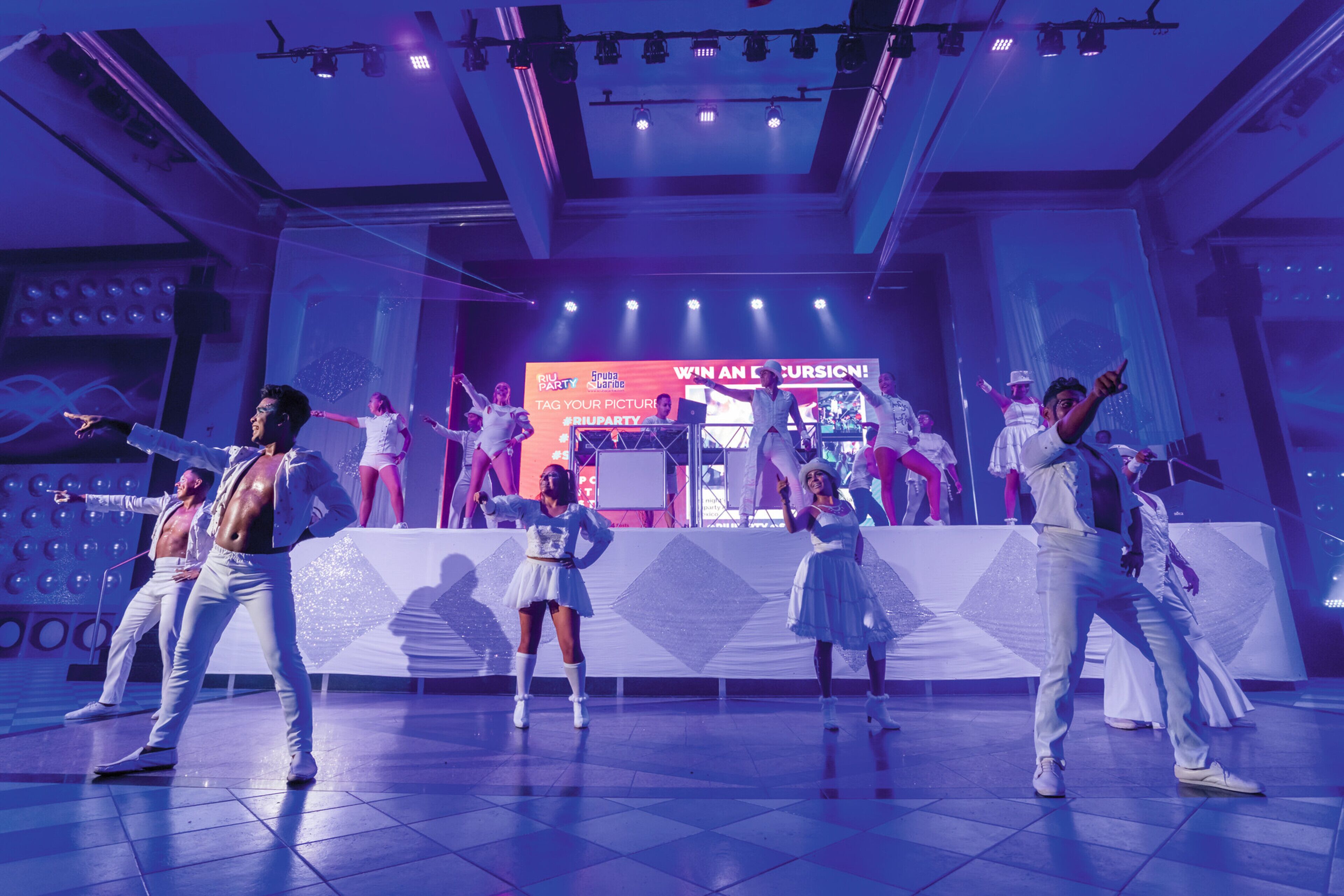 A dance performance on a stage with a backdrop displaying "SPOT PARTY" and "WE'RE AN OCCASION!" text.