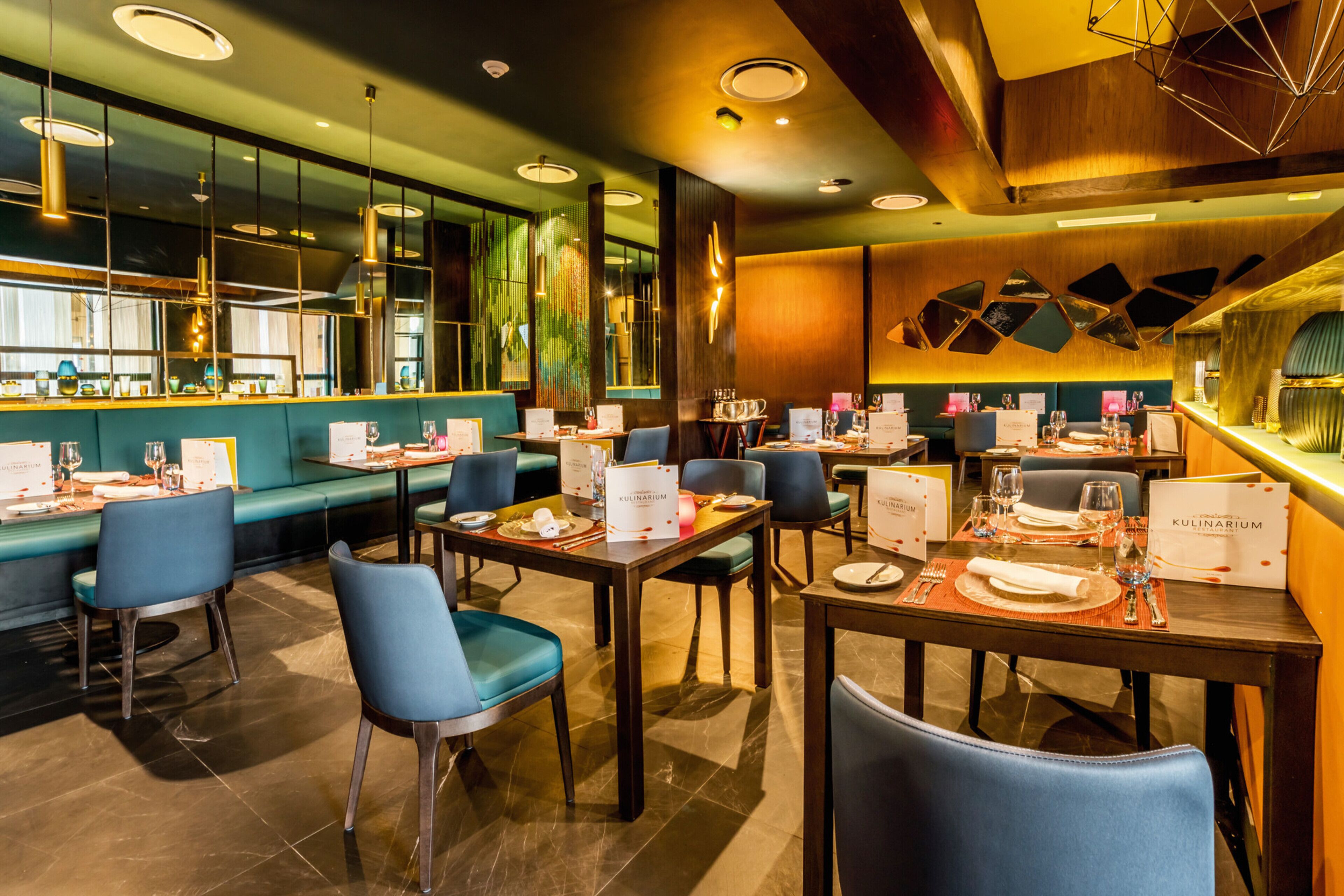 Un restaurante con varias mesas y sillas, una zona de bar y un espacio de estar con un banco acolchado verde.