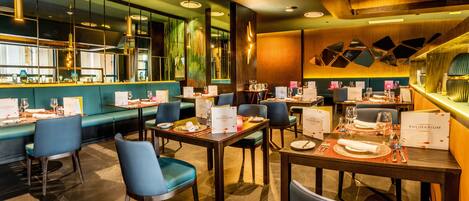 Un restaurante con varias mesas y sillas, una zona de bar y un espacio de estar con un banco acolchado verde.