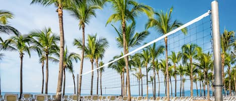 Una red de voleibol de playa con palmeras y sillas de playa al fondo.