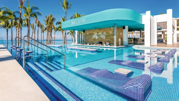A pool area with lounge chairs, a bar, and a view of the ocean. - Hotel Riu Vallarta - All Inclusive (Nuevo Nayarit)