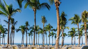 A beach with rows of white lounge chairs and palm trees. - Hotel Riu Vallarta - All Inclusive (Nuevo Nayarit)