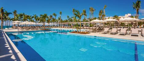 A clear blue pool with lounge chairs and umbrellas, surrounded by palm trees.
