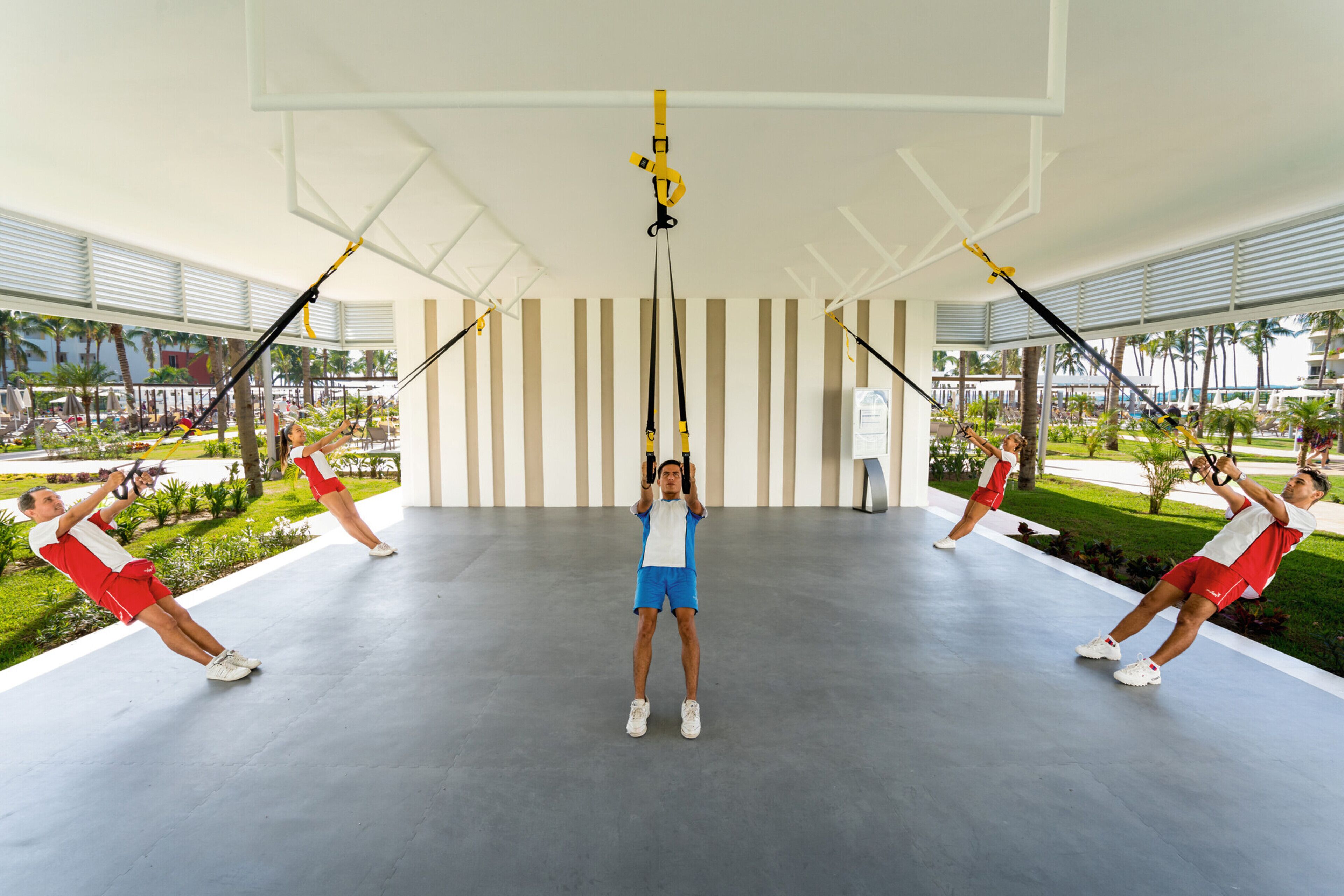 A spacious indoor area with a modern design, featuring a central suspended exercise equipment and multiple people using it.