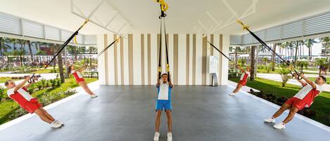 A spacious indoor area with a modern design, featuring a central suspended exercise equipment and multiple people using it.