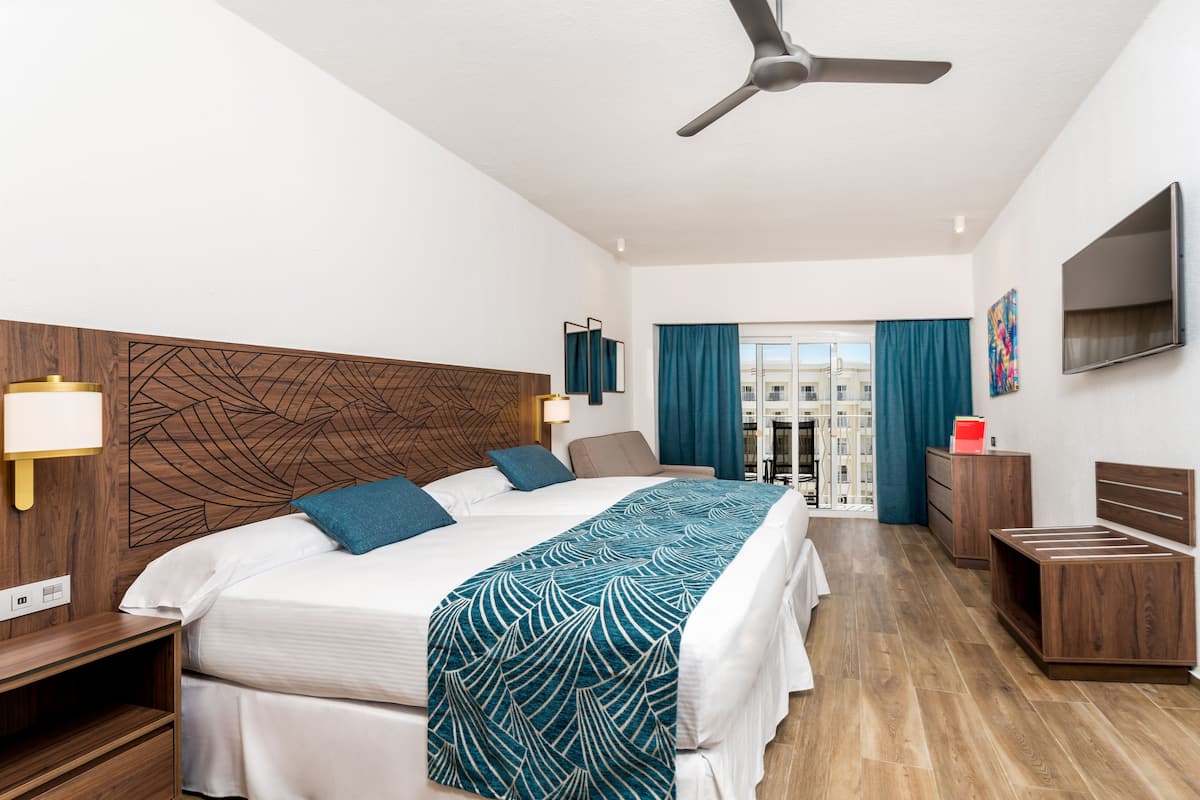 Habitación de hotel moderna con una cama grande, ventilador de techo, televisión y vista a la ciudad desde la ventana.