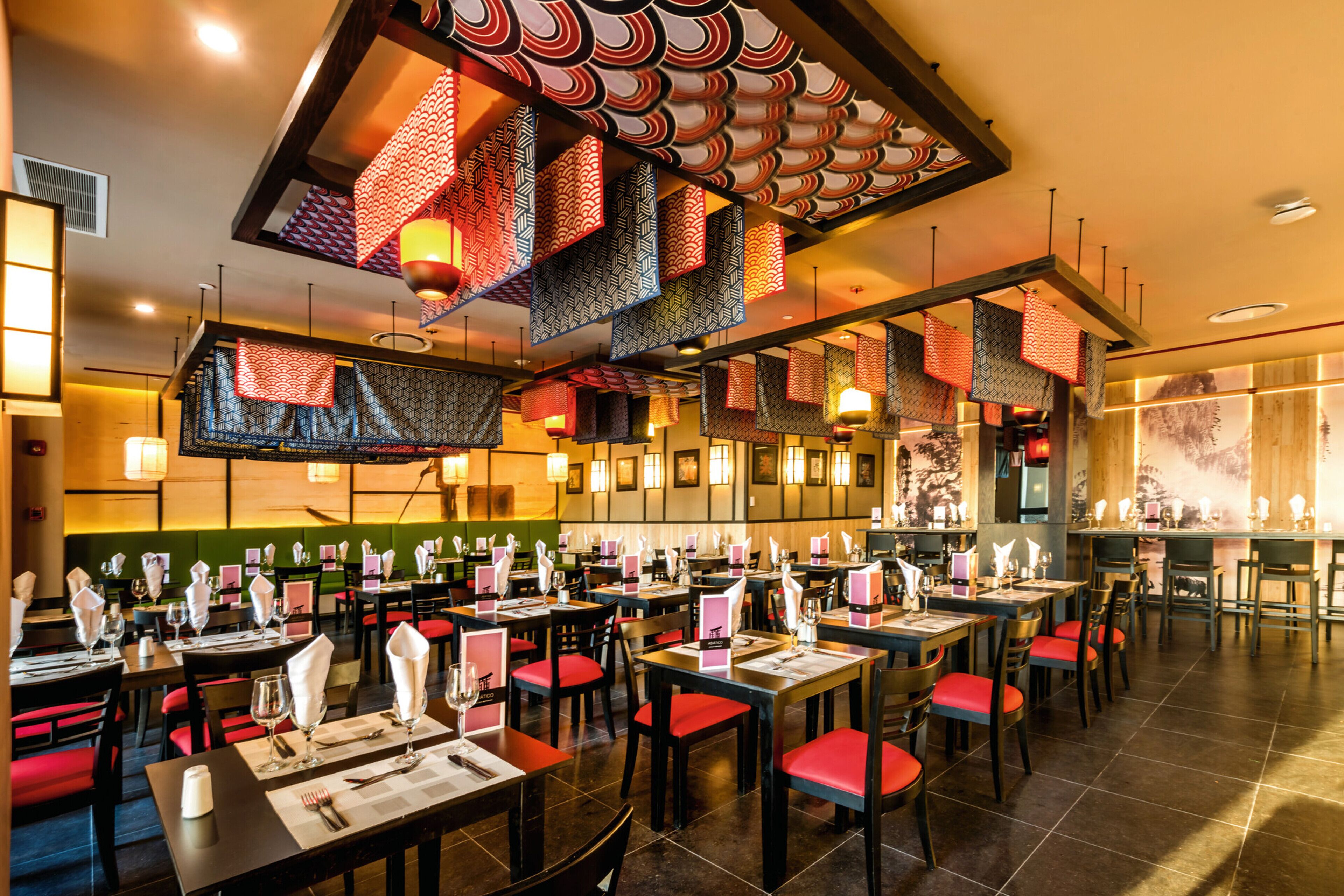 Een restaurant met meerdere tafels en stoelen, waarvan sommige rode kussens hebben.
