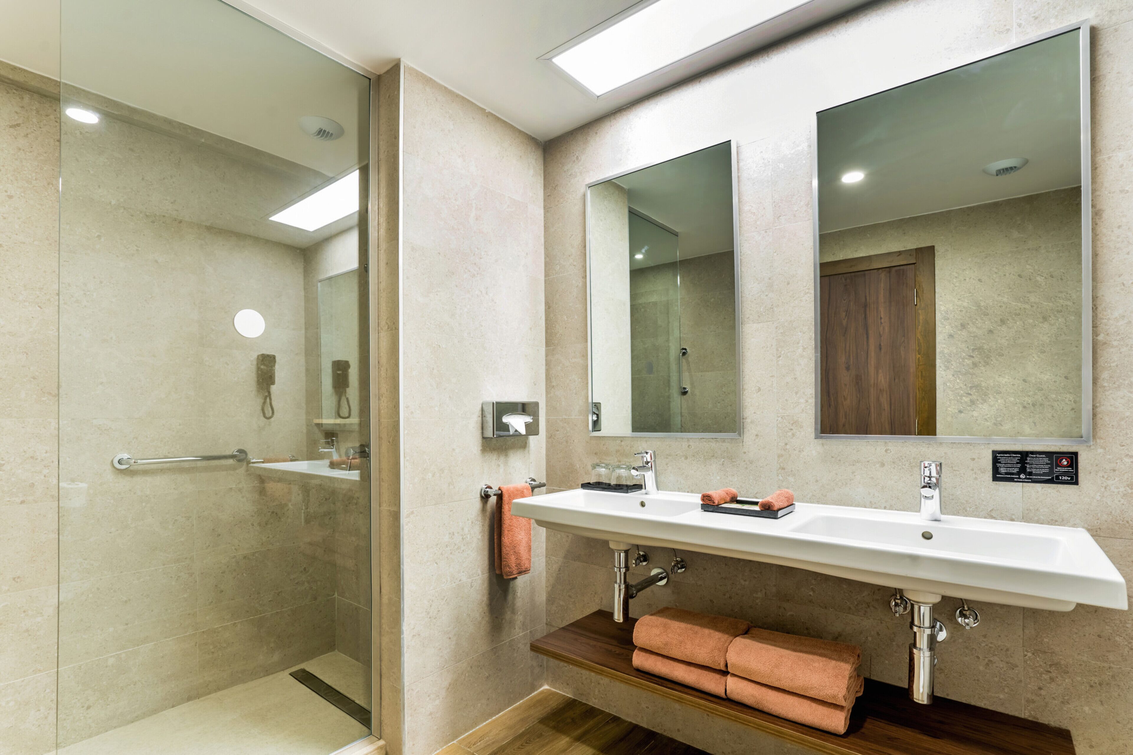 Un baño moderno con cabina de ducha de vidrio, un lavamanos grande con espejo y un mueble de tocador de madera.