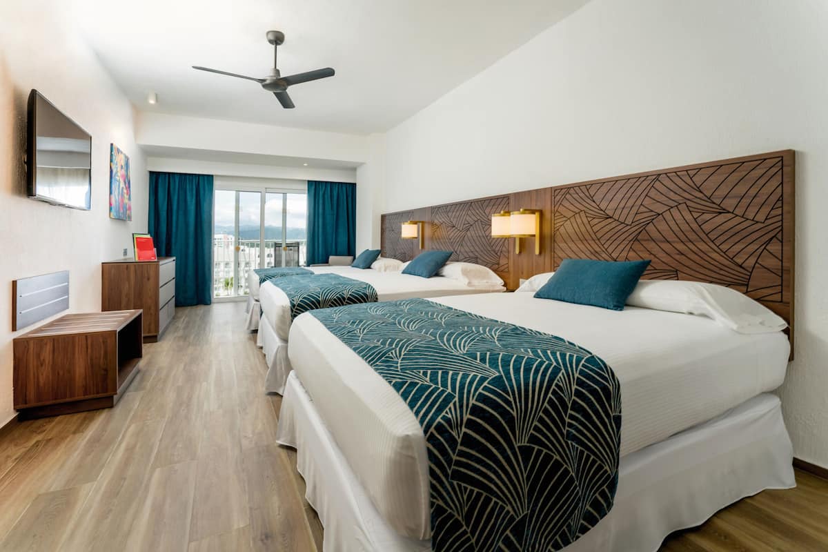 Habitación de hotel con dos camas, un escritorio, un ventilador de techo y un ventanal grande con cortinas.