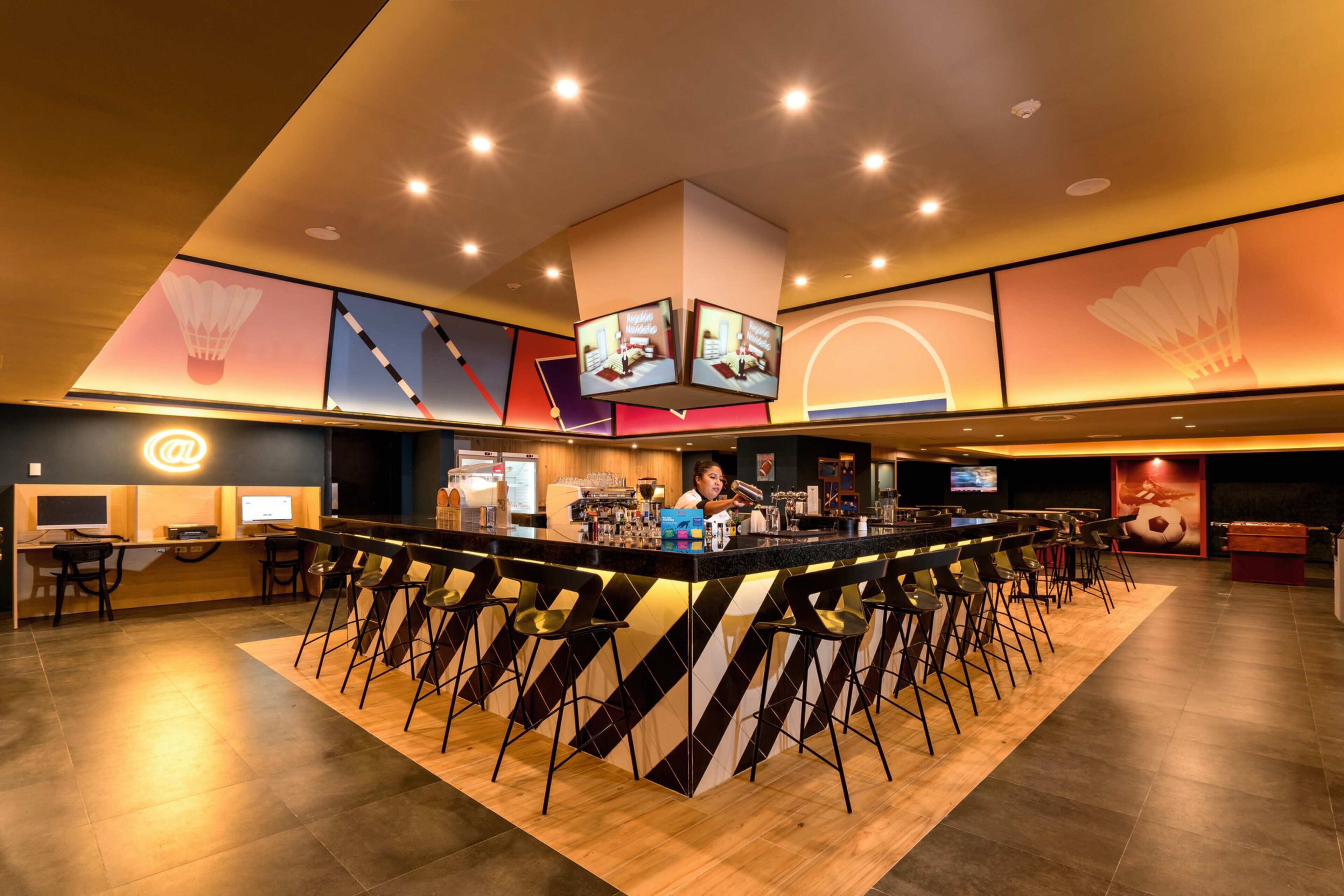 Un área de bar moderna con un mostrador central, varias pantallas y un conjunto de asientos.