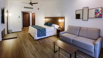 Una habitación de hotel con una cama, un sofá, una mesa de centro, un ventilador de techo y un televisor montado en la pared.