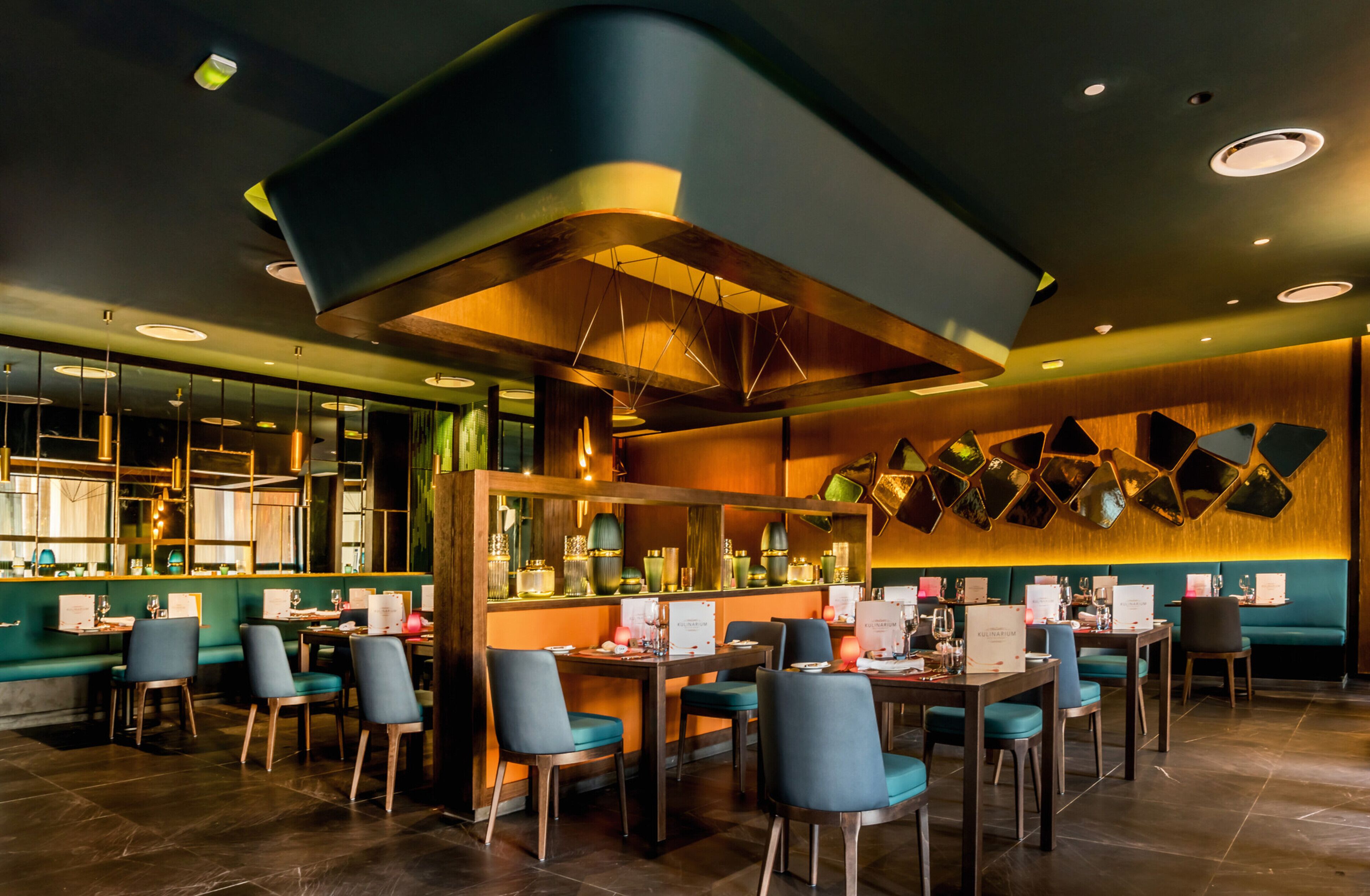 A restaurant with a modern interior, featuring a curved ceiling, green seating, and a bar area.
