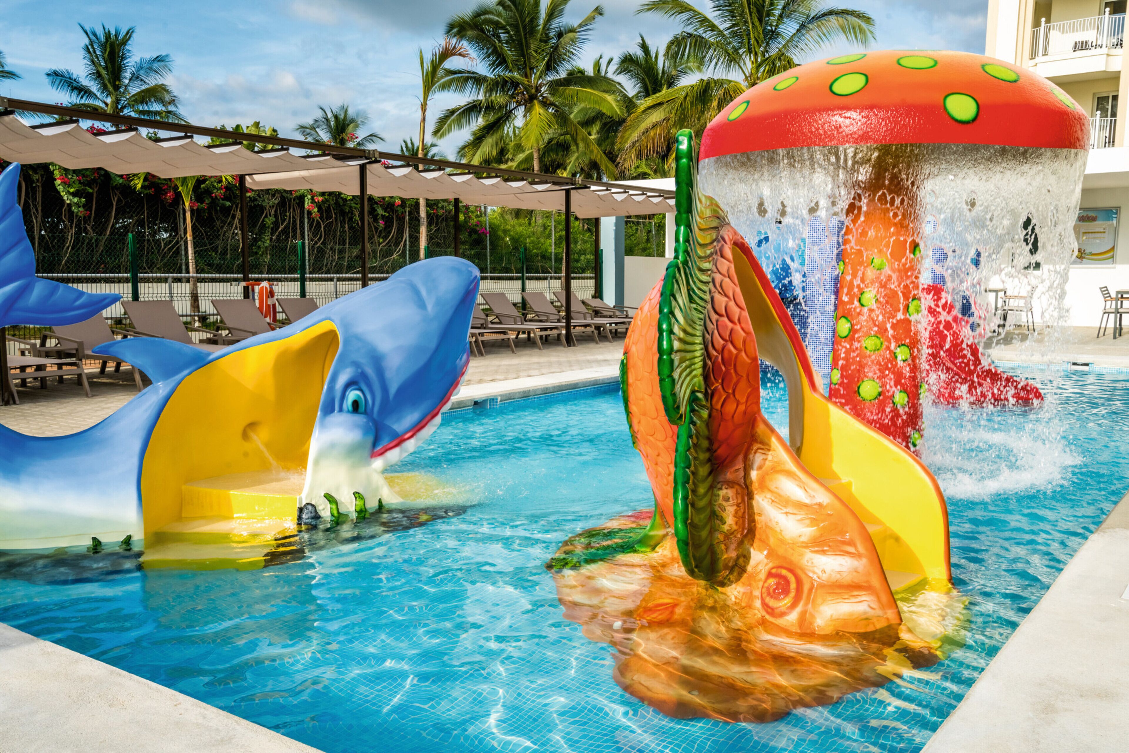 A swimming pool with a slide shaped like a fish and a mushroom.