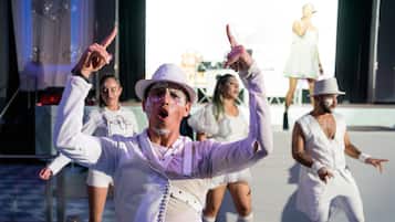 A group of people in white outfits performing on a stage with a large screen in the background.
