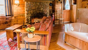 A cozy cabin interior with a stone fireplace, a sofa, a wooden table with a vase, and a bathtub. - Arrowhead Inn (Durham)