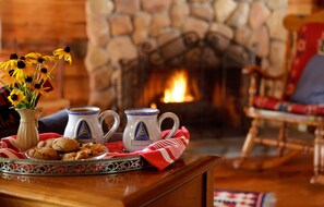 A cozy room with a fireplace, a table with cookies, mugs, and a vase of flowers.